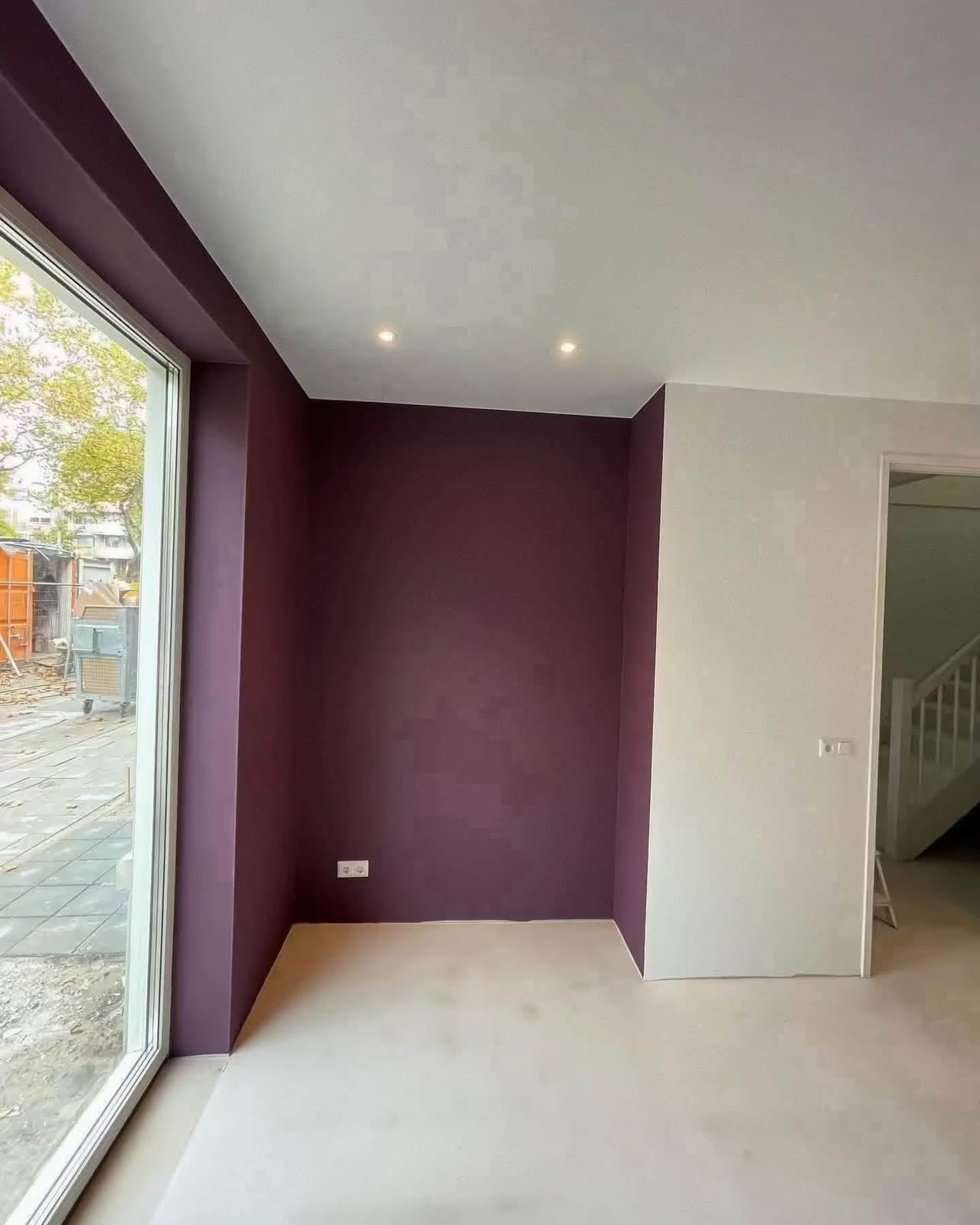 Strak geschilderde accentwand in diep aubergine naast een groot raam