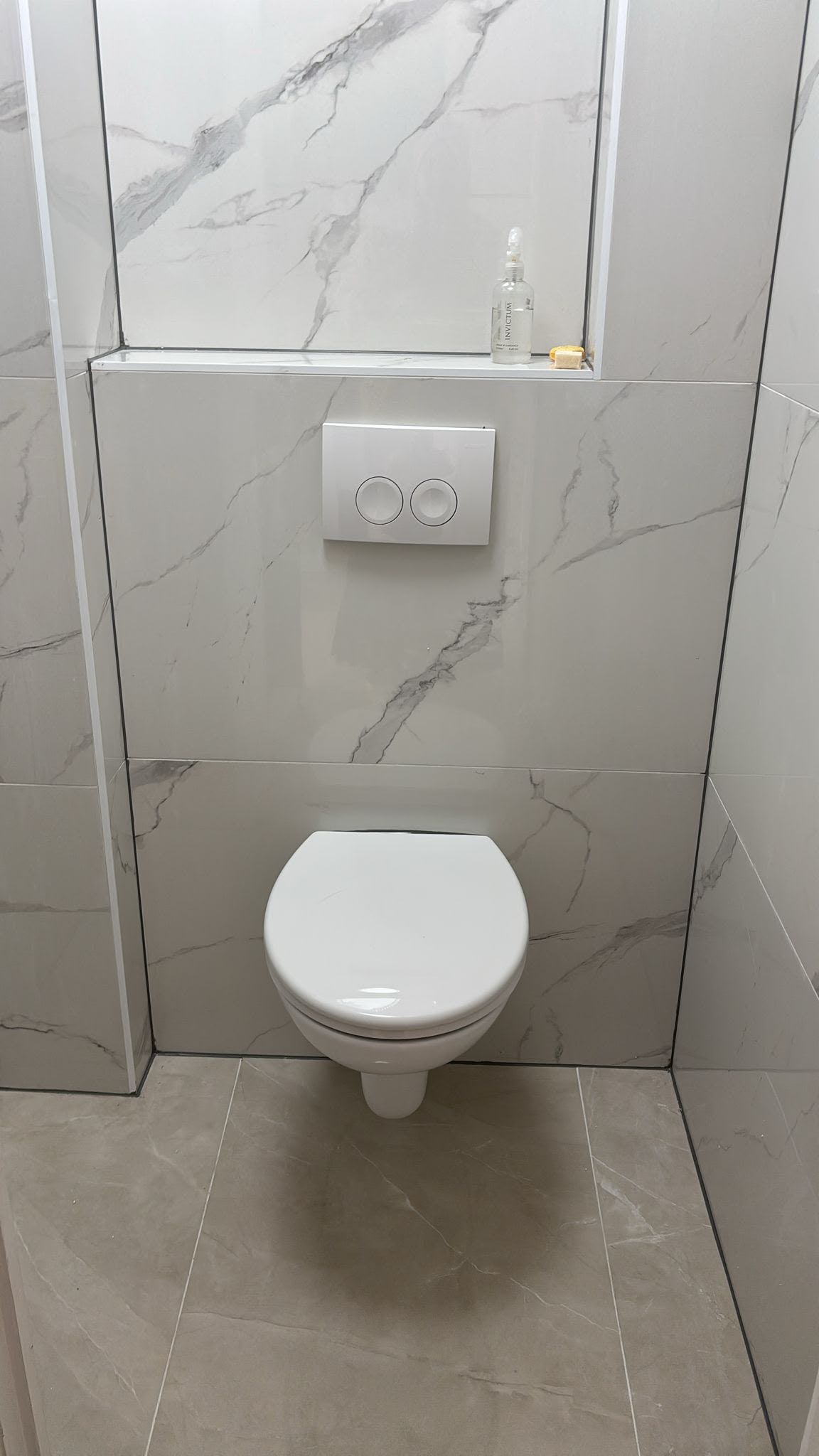 Toilet met hangtoilet, inbouwreservoir, marmerlook wandtegels en een tegelnis
