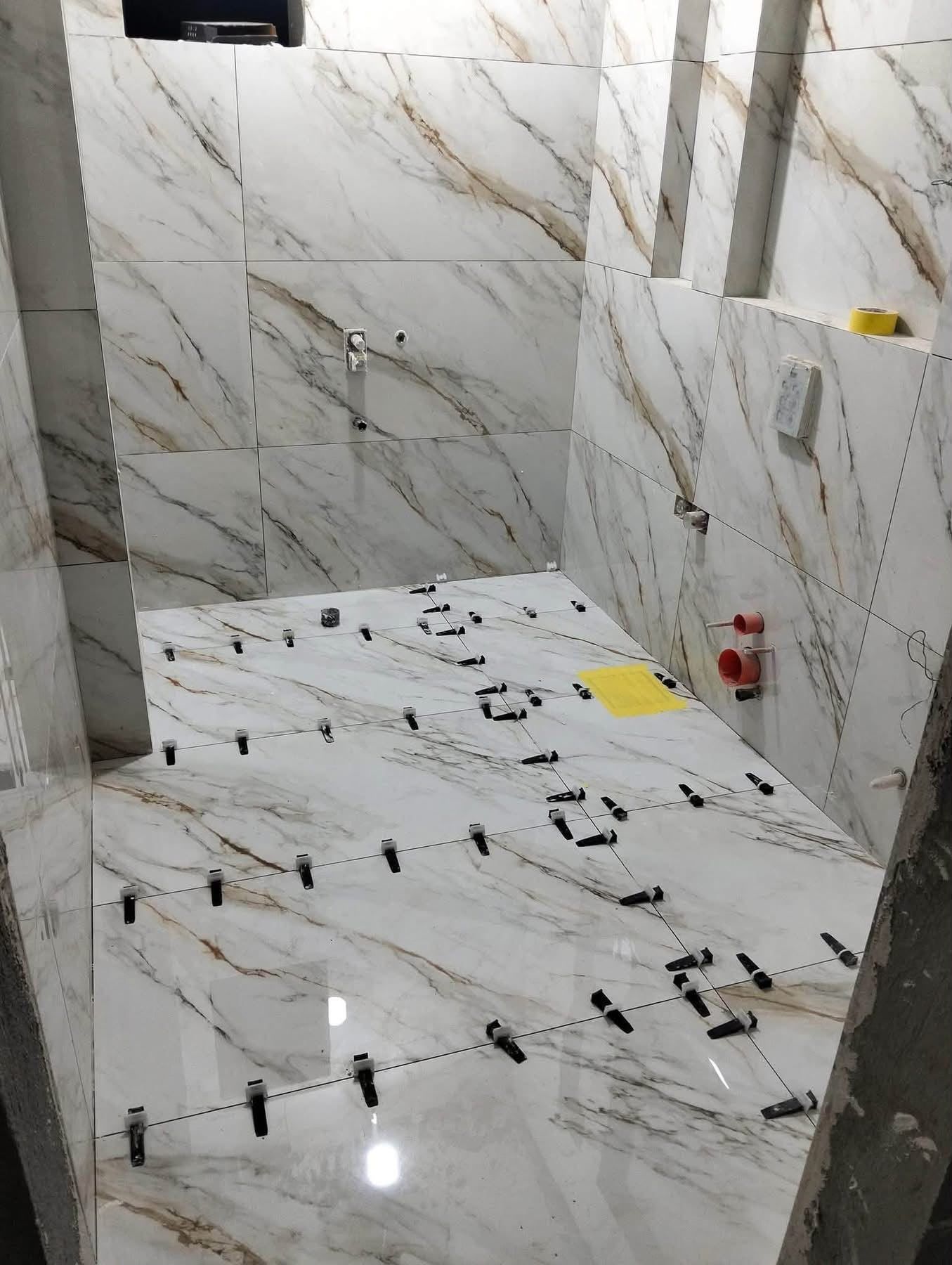 Badkamer in aanbouw met grootformaat marmerlook tegels op vloer en wanden, met tegelnivelleersysteem