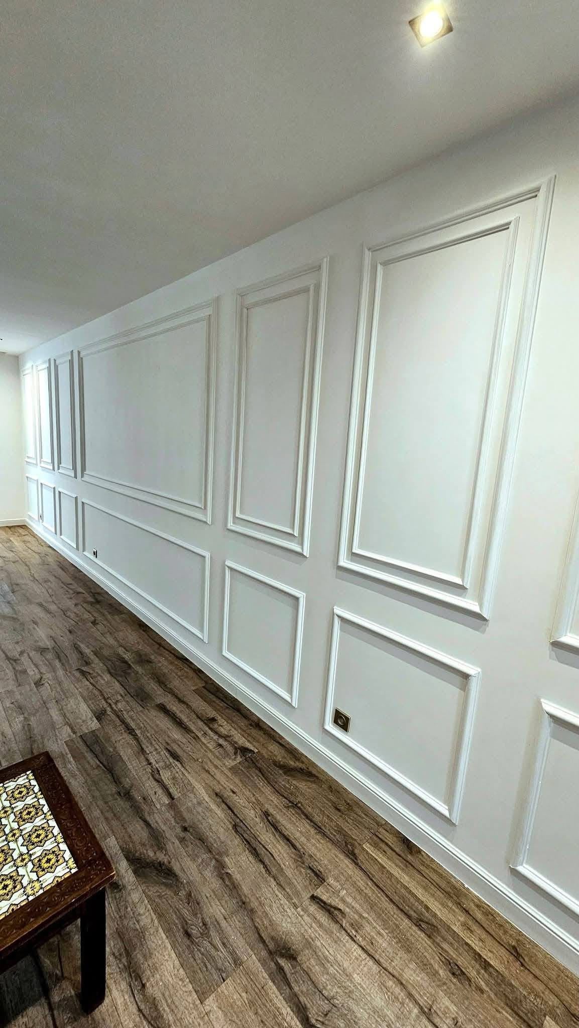 Lange gang met witte klassieke wandlijsten en een houten vloer