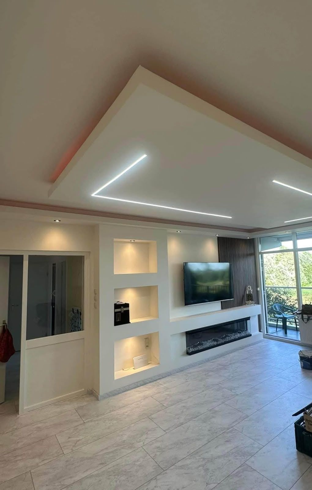 Woonkamer met verlaagd plafond met LED-lijnen, verlichte wandnissen, haard en tv-wand